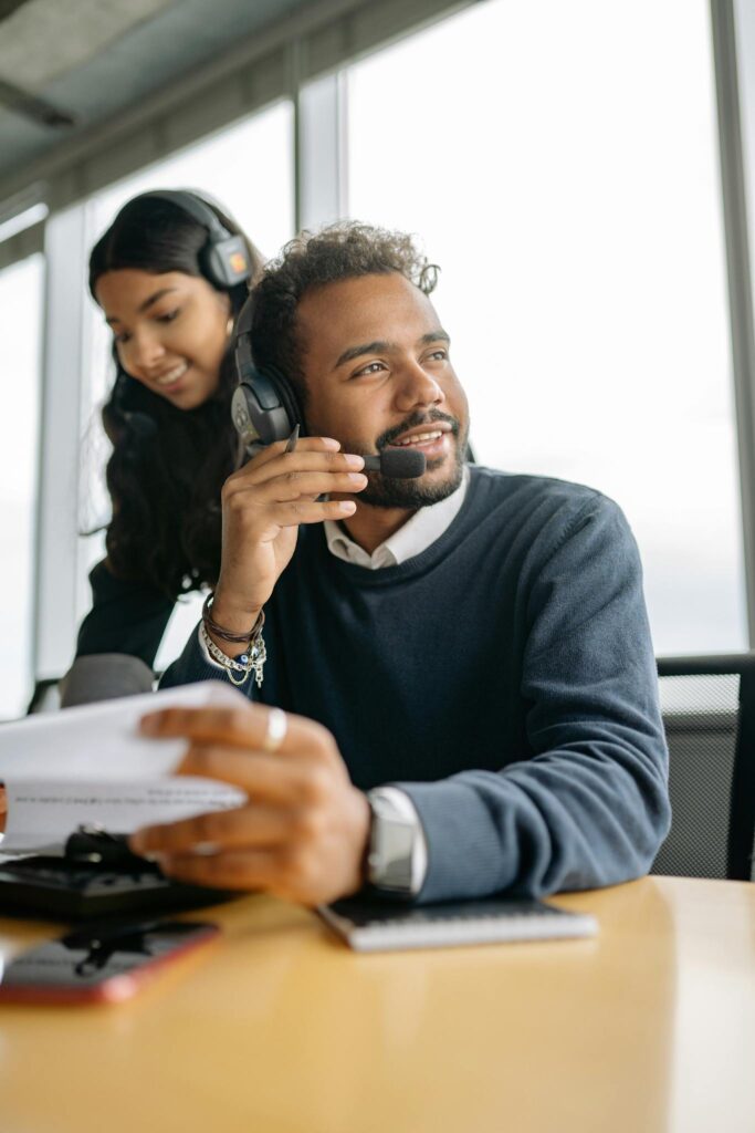 Two call center agents using headsets, working together at a desk in an office setting.